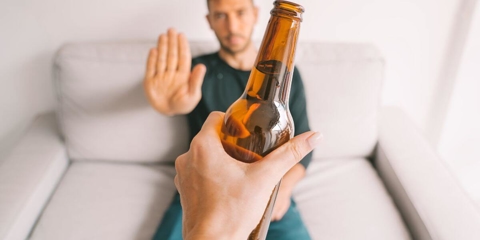 man in his thirties sitting on a couch and putting his hand up to decline a beer