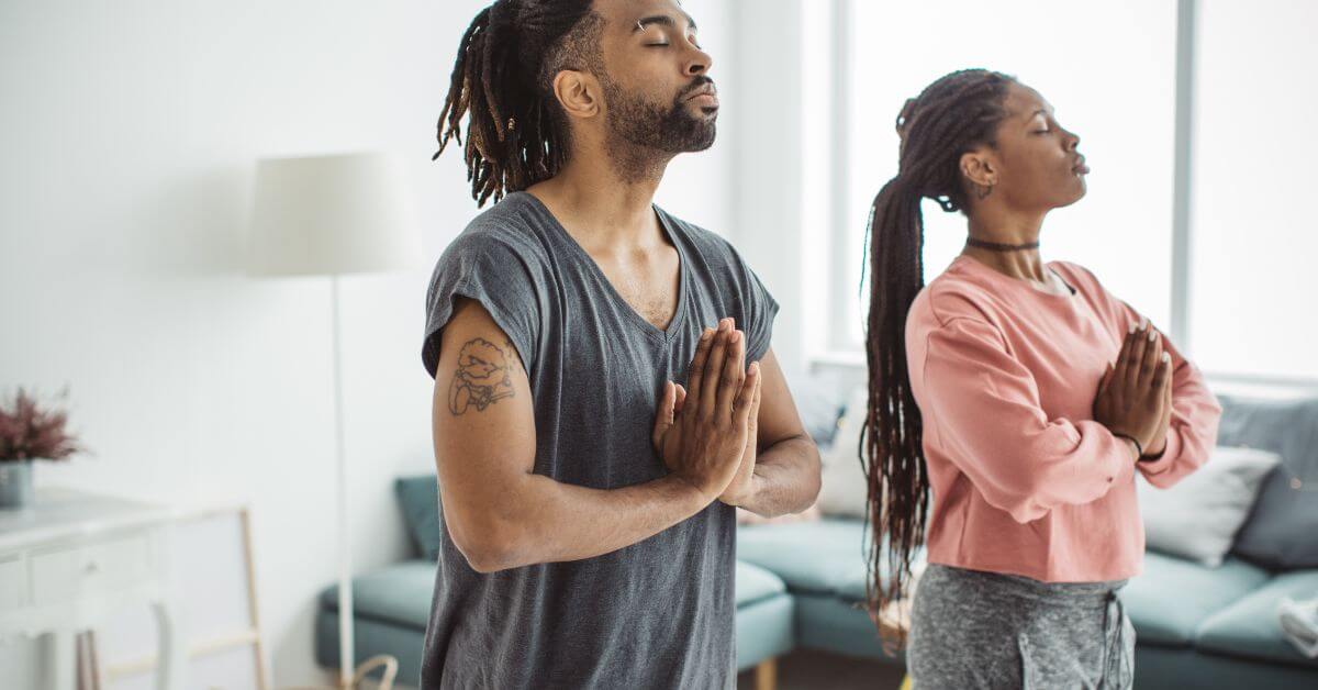 black man and woman standing with eyes clothes and holding their hands together while meditating