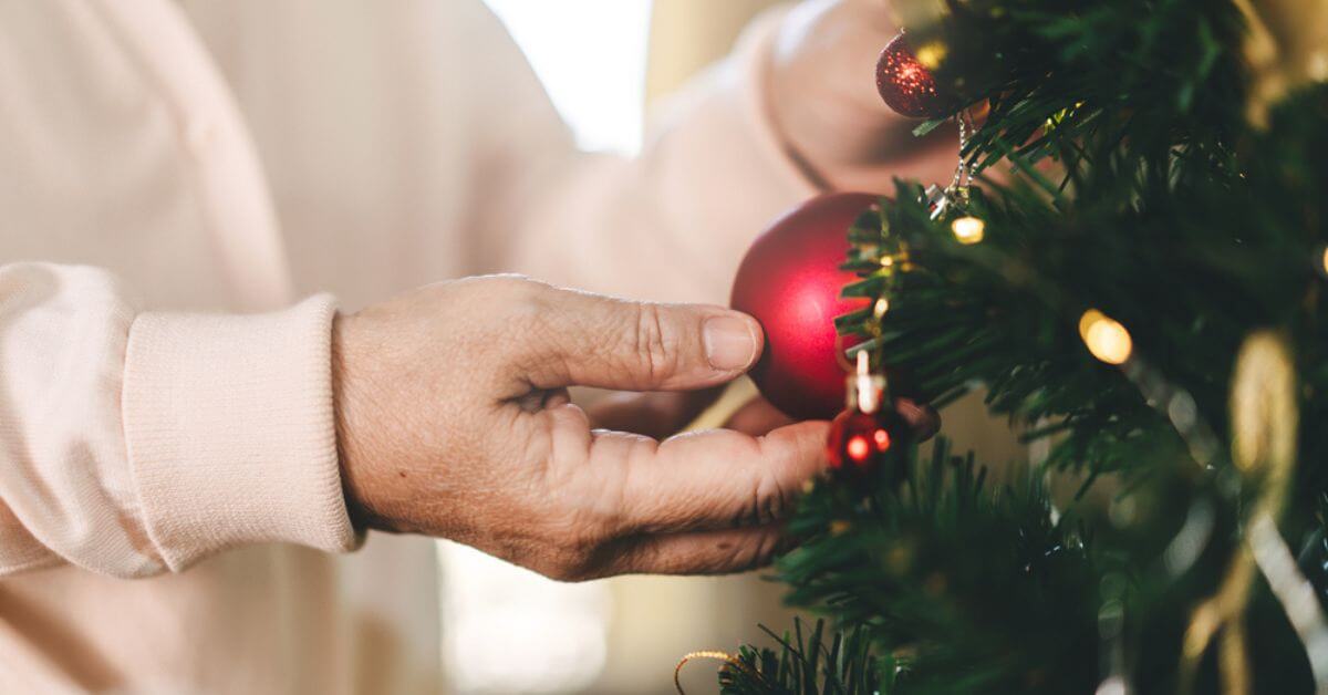 older woman putting a red ornament on a christmas tree