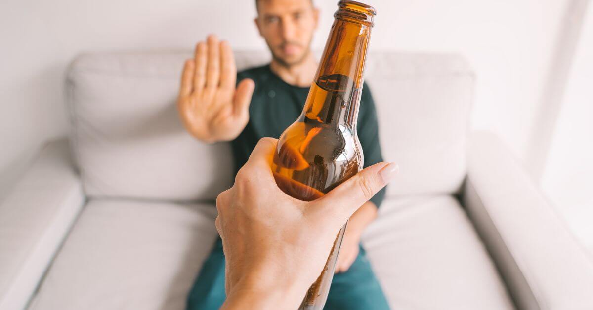 man in his thirties sitting on a couch and putting his hand up to decline a beer